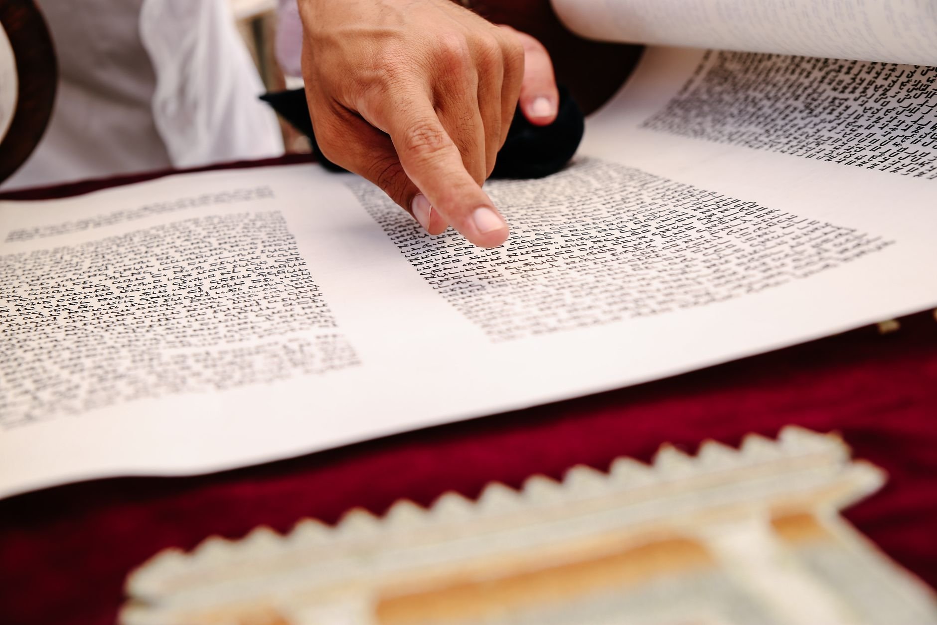 A close-up view of a hand pointing to text on an ancient religious scroll, indicating reading and study.
